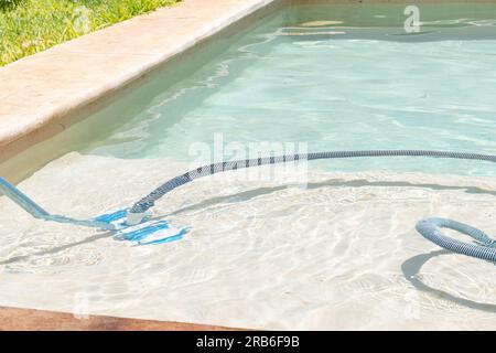 Pulizia della piscina con l'aspirapolvere durante una giornata di sole. Piscina in stile Chucum Foto Stock