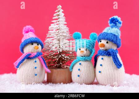 Tre pupazzi di neve a maglia su sfondo magenta con cappelli blu e rosa. Buon Natale e Capodanno 2024 biglietto d'auguri Foto Stock