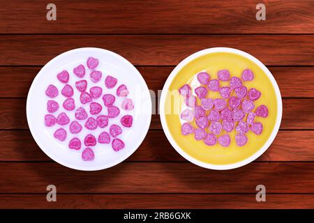 Due piatti con caramelle a forma di cuore su sfondo di legno Foto Stock