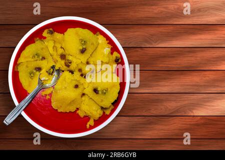 Dessert tradizionale indiano kesari con uva passa su piatto rosso su tavolo di legno. Foto Stock