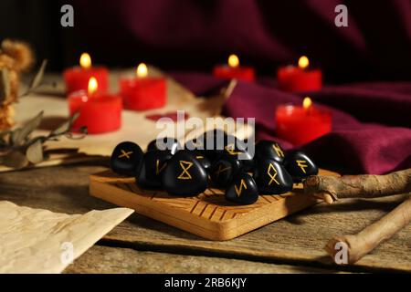 Molte pietre runiche nere e candele brucianti su un tavolo di legno, primo piano Foto Stock