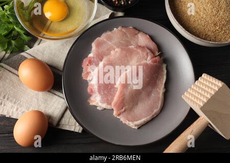 Cottura dello schnitzel. Fette di maiale crude, altri ingredienti e tenerizzatore di carne su tavola di legno, spianata Foto Stock