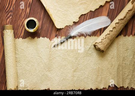 Primo piano del rotolo e del quill vicino alla pentola d'inchiostro su un tavolo di legno Foto Stock