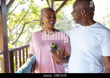 Ritratto di una felice coppia afroamericana anziana che tiene un tappetino per esercizi yoga sulla terrazza. Senior lifestyle, relax, pensione, vita sana, fitness, Foto Stock