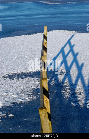 Lunghe ombre di recinzione in legno che vengono gettate dal sole di Winters a Murton Lochs sopra l'acqua ghiacciata coperta dalla neve. Foto Stock