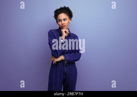 ritratto di una giovane donna bruna ispanica con morbidi capelli ricci in abito in denim blu Foto Stock