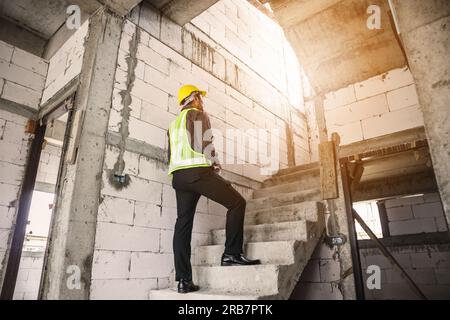 giovane ingegnere professionista in casco protettivo e blueprints carta a portata di mano presso il cantiere di costruzione della casa Foto Stock