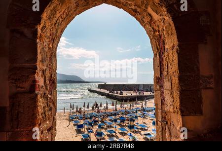 Arco attraverso un antico edificio in pietra che conduce ad una spiaggia con persone irriconoscibili a Cefalù, Sicilia, Italia Foto Stock