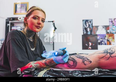 Tatuatrice sicura di sé che guarda la fotocamera mentre lavora a un nuovo progetto. Interni dello studio di tatuaggio. Foto di alta qualità Foto Stock