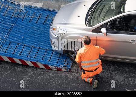 Galizia, Spagna; 8 luglio 2023: Operatore dell'assistenza stradale che solleva un'auto sul veicolo trainato. Servizio di traino sul ci Foto Stock