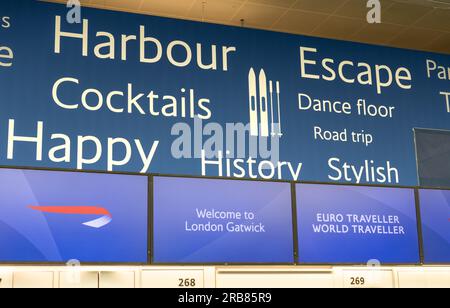 Parole che promuovono la felicità del viaggio dietro i banchi di check-in della British Airways all'aeroporto Gatwick di Londra, South Terminal, West Sussex, Regno Unito. Foto Stock