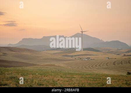 Paesaggio idilliaco all'alba della campagna di Malaga, Andalusia, Spagna, con prati, montagne sullo sfondo e un mulino a vento Foto Stock