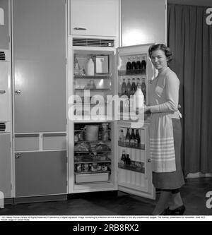 In cucina anni '1960 Una donna nella sua cucina con la porta aperta sul frigorifero. Puoi vedere i prodotti alimentari di vari tipi che sono ordinatamente esposti sugli scaffali. Tra le altre cose, è visibile il classico pacchetto di latte Tetran. Inventato da Ruben Rausing e che divenne l'inizio dell'impero del packaging Tetra Pak. Svezia 1960. Rif. Conard 4188 Foto Stock