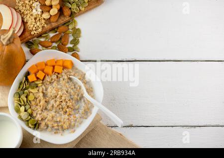 Porridge di farina d'avena con zucca e semi di zucca, noci su sfondo bianco. Cibo sano con spazio per copiare Foto Stock