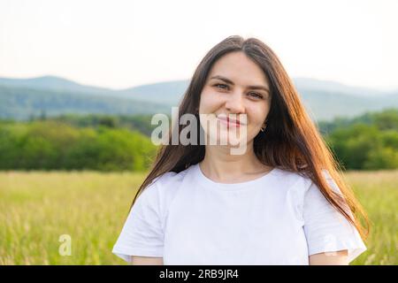 Ritratto di una donna europea di 30 anni che sorride mentre guarda la fotocamera mentre cammina nella natura in un campo. Foto Stock