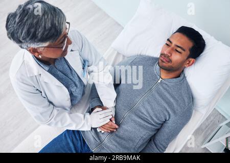 Malato, sopra e medico che tiene per mano un uomo in un ospedale per supporto, consulenza e cura. Sanità, letto e una persona medica matura con Foto Stock