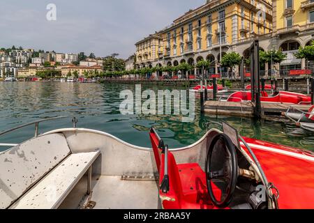 Divertenti barche rosse a forma di auto da corsa sul lago di Lugano, in Svizzera, con la città sullo sfondo Foto Stock