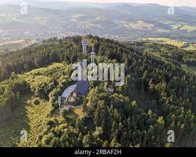 Vista aerea della cima della collina di Svatobor con una storica torre panoramica con una capanna turistica, una torre di telecomunicazioni e una torre di conversione TV Foto Stock