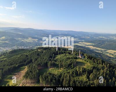 Vista aerea della cima della collina di Svatobor con una storica torre panoramica con una capanna turistica, una torre di telecomunicazioni e una torre di conversione TV Foto Stock