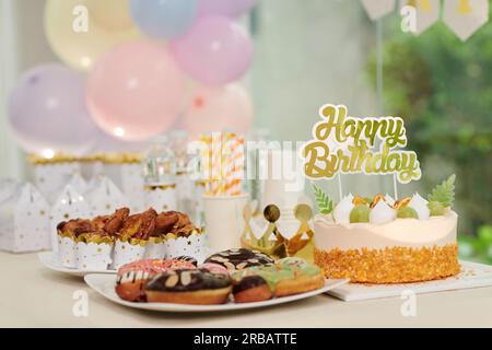 Torta di compleanno decorata, ciambelle e cupcake sul tavolo preparati per gli ospiti della festa Foto Stock