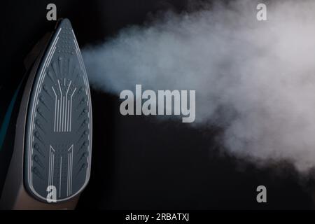 Ferro visto dalla parte anteriore con vapore che fuoriesce dai suoi orifizi su sfondo nero Foto Stock