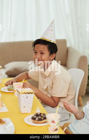 Sorridente preteen asiatico ragazzo che mangia dolci alla festa di compleanno Foto Stock