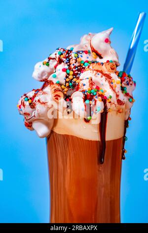 Caffè freddo con panna montata, spruzzi di zucchero e salsa al cioccolato, primo piano, sfondo blu Foto Stock