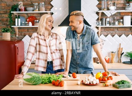 Sorridente giovane coppia che cucinano insieme pasto vegetariano in cucina a casa. Donna che abbraccia l'uomo. Concetto di stile di vita sano Foto Stock