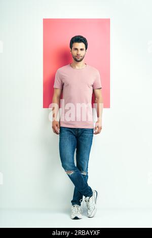 Ritratto a lunghezza intera di un giovane bell'uomo con t-shirt rosa su sfondo geometrico Foto Stock