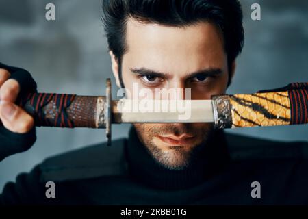 Uomo guerriero in posa con una spada isolata su sfondo nero. Primo piano verticale Foto Stock