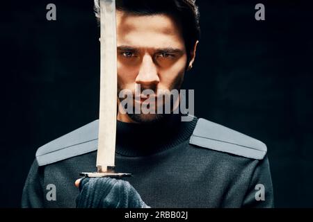 Uomo guerriero in posa con una spada isolata su sfondo nero. Primo piano verticale Foto Stock