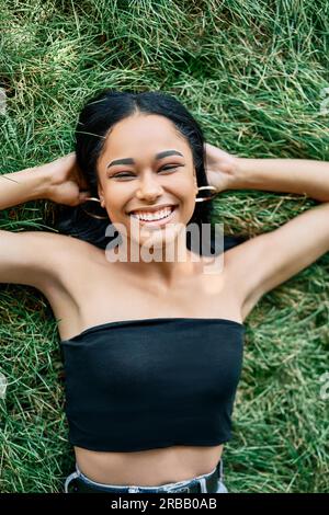 Vista dall'alto ritratto di una donna afro-americana piuttosto felice che si rilassa sull'erba nel parco. Riposo, concetto di bellezza femminile Foto Stock