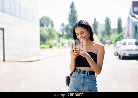 Felice donna nera sorridente che guarda il suo smartphone che cammina in città. Persone, concetto di comunicazione Foto Stock