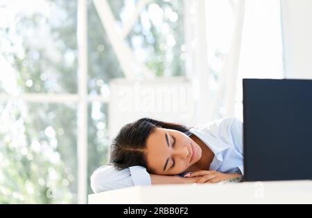 Donna d'affari stanca e in eccesso che dormiva sul posto di lavoro sulla scrivania dell'ufficio Foto Stock
