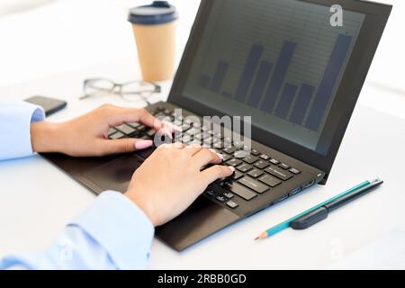 Primo piano le mani della donna che scrivano su un computer portatile. Businesswoman guarda grafico analisi statistica dei dati finanziari in ufficio moderno Foto Stock