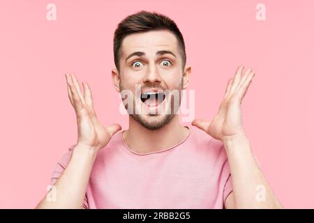 Primo piano ritratto di uomo sorpreso e stupito con braccia sollevate su sfondo rosa. Emozioni, successo, concetto vincitore Foto Stock