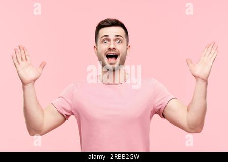 Ritratto emozionato sorpreso uomo con braccia sollevate su sfondo rosa. Emozioni, successo, concetto vincitore Foto Stock