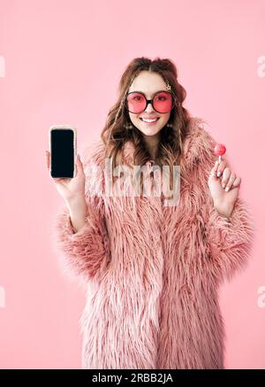 Donna hipster sorridente che tiene nero schermo telefono cellulare su sfondo rosa Foto Stock