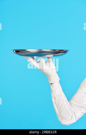 Elegante mano del cameriere in guanto bianco che tiene il vassoio in metallo su sfondo blu. Ristorante, horeca, concetto di servizio di prima classe Foto Stock