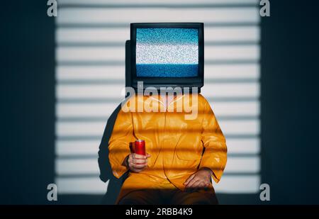 Arte surreale di un uomo dipendente dalla TV con la televisione invece che la testa. Concetto zombie media con uomo in impermeabile giallo brillante che regge una soda dolce in rosso Foto Stock