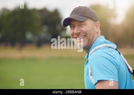 Sorridente golfer amichevole di mezza età che si gira per guardare indietro sopra il suo spalla alla fotocamera sul fairway o verde Foto Stock