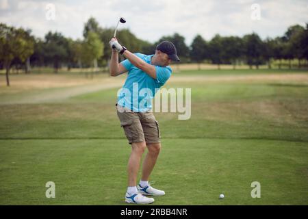 Un uomo gioca a golf e alza la palla mentre guarda il fairway da dietro con un autista, in un concetto per uno stile di vita sano e attivo Foto Stock