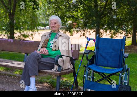 Ritratto di una donna anziana seduta su una sedia nel giardino di una casa di cura su una sedia a rotelle Foto Stock