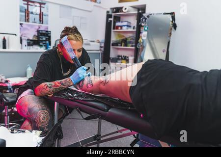 maestro del tatuaggio concentrato che lavora su un nuovo tatuaggio su una gamba, studio di tatuaggio. Foto di alta qualità Foto Stock