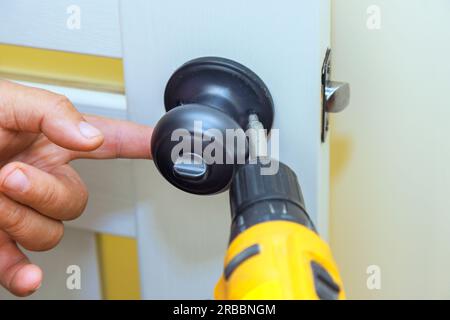 Il lavoratore installa la serratura nella nuova porta interna con un cacciavite Foto Stock