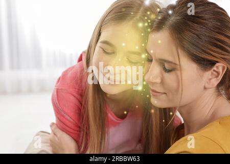 Empatia. Madre che abbraccia la sua figlia adolescente pacificata al chiuso. Luci tra di loro come simbolo di sostegno emotivo e comprensione Foto Stock