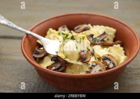 Deliziosi ravioli con funghi e forchetta su tavolo in legno, primo piano Foto Stock