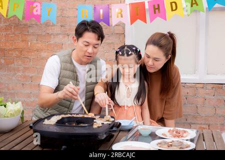 Padre e madre e figlia della famiglia asiatica che mangiano cibo al ristorante mentre festeggiano il compleanno, mamma e papà mangiano con piacere in vacati Foto Stock