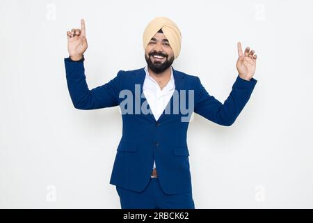 Allegro uomo d'affari indiano sikh che indossa abiti che ballano con gioia isolato su sfondo bianco. Concetto aziendale. Foto Stock