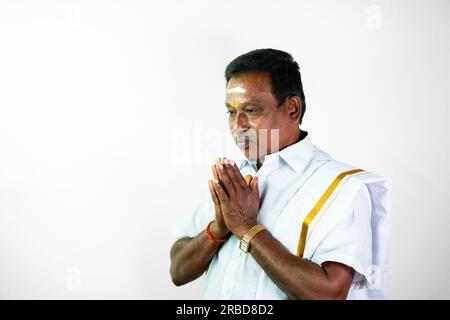 Un uomo dell'India del sud, di 50 anni, che indossa un dothi bianco tradizionale e una camicia bianca, saluta con il gesto del vanakkam. Sta alzando le mani in un Foto Stock